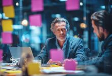 جلسه کوچینگ مدیریتی در فضای اداری مدرن؛ گفت‌وگوی دو مدیر کنار لپ‌تاپ و یادداشت‌های چسبی برای شفاف‌سازی اولویت‌ها و تصمیم‌گیری نتیجه‌محور.