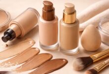 لوازم آرایشی مرتبط با کرم‌پودر شامل بطری‌های کرم‌پودر در چند تناژ مختلف، سواچ‌های رنگی روی سطح، پودر فیکس، اسفنج آرایشی و براش‌ها در یک چیدمان مینیمال و روشن